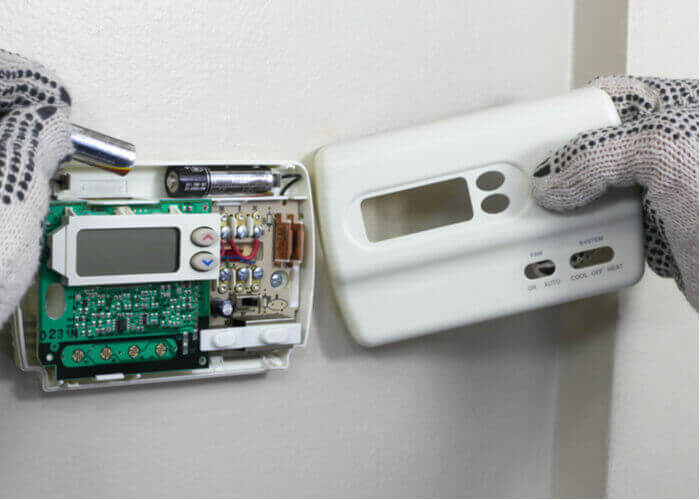 image shows person replacing the batteries in a thermostat